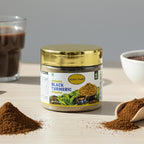 Jar of organic black turmeric powder with a gold lid on a wooden surface, surrounded by turmeric powder and a glass of dark liquid.